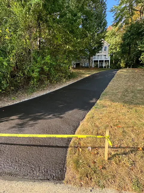 Freshly laid asphalt driveway edge with gravel shoulder and caution tape