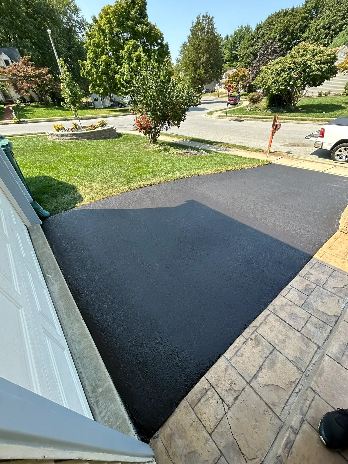 Black sealcoated driveway next to a stamped concrete walkway