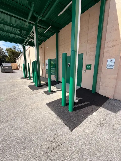 Freshly sealed asphalt under a loading canopy with green bollards