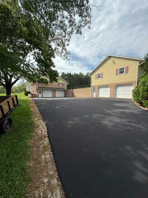 Wide sealcoated driveway in front of a yellow house with a three-car garage